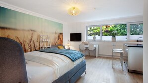Un dormitorio con cama, escritorio, silla, televisor y ventana con vistas a zonas verdes.