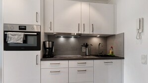 Una cocina moderna con electrodomésticos de acero inoxidable, armarios blancos, horno empotrado y cafetera.