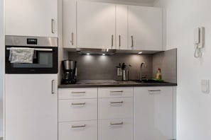 A modern kitchen with stainless steel appliances, white cabinetry, a built-in oven, and a coffee maker.