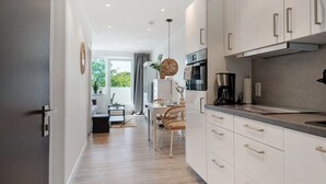 Una cocina moderna con armarios blancos, un comedor con mesa y sillas, y vista a zonas verdes.