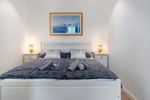 A neatly made bed with a patterned bedspread, two bedside lamps, a framed picture on the wall, and a white headboard. - Apartment 'Ferienappartement Holm Ostsee' with Balcony and Wi-Fi (Schönberg-Holm)