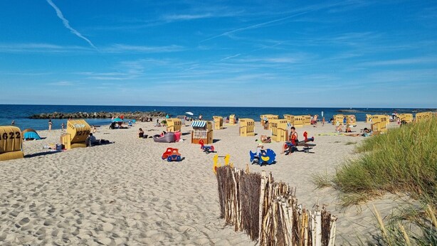 Una playa con numerosas cabañas de playa amarillas, algunas con números, y algunas personas al fondo.