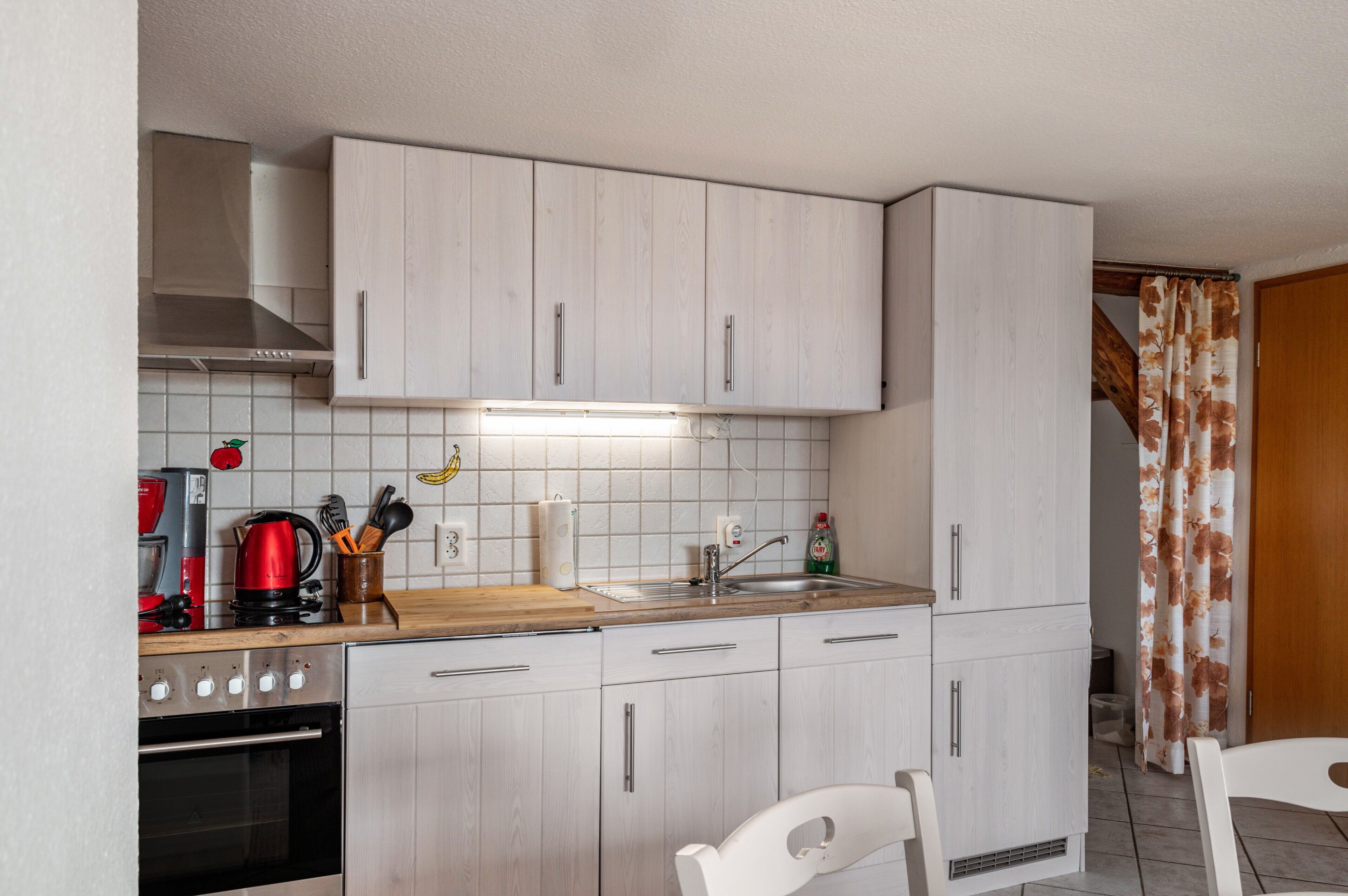 Une cuisine compacte avec des meubles blancs, une hotte de cuisinière en acier inoxydable, un four encastré, un évier et un plan de travail en bois.