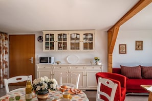 A dining area with a table set for two, a cabinet with glass doors, a red sofa, and a microwave on a cabinet. - Apartment "Zur Eule - Uhu" with Shared Garden & Wi-Fi (Satow OT Clausdorf)
