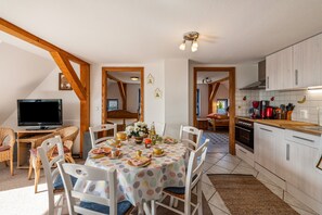 Un comedor con mesa dispuesta para seis, televisor y cocina con muebles blancos y encimera de madera.