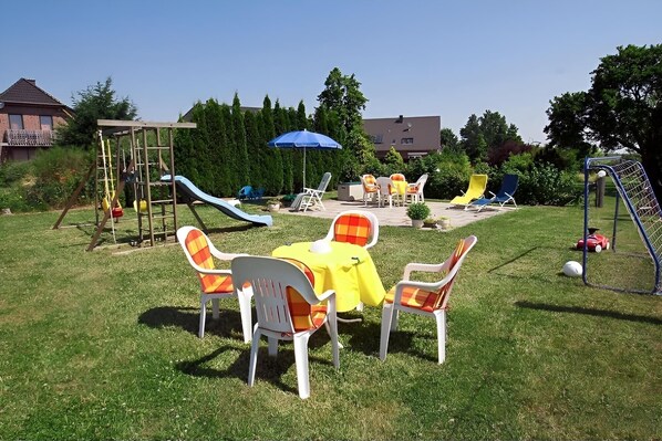 A backyard with a play area, including a slide and climbing structure, and a seating area with chairs and a table. - Apartment "Zur Eule - Uhu" with Shared Garden & Wi-Fi (Satow OT Clausdorf)
