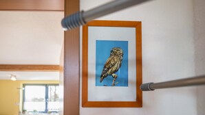 A framed owl artwork on a wall, a window with a view, and a room with a table and chairs.