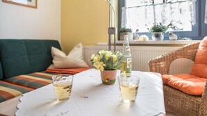 A cozy room with a sofa, a wicker chair, a table with drinks and a flower pot.