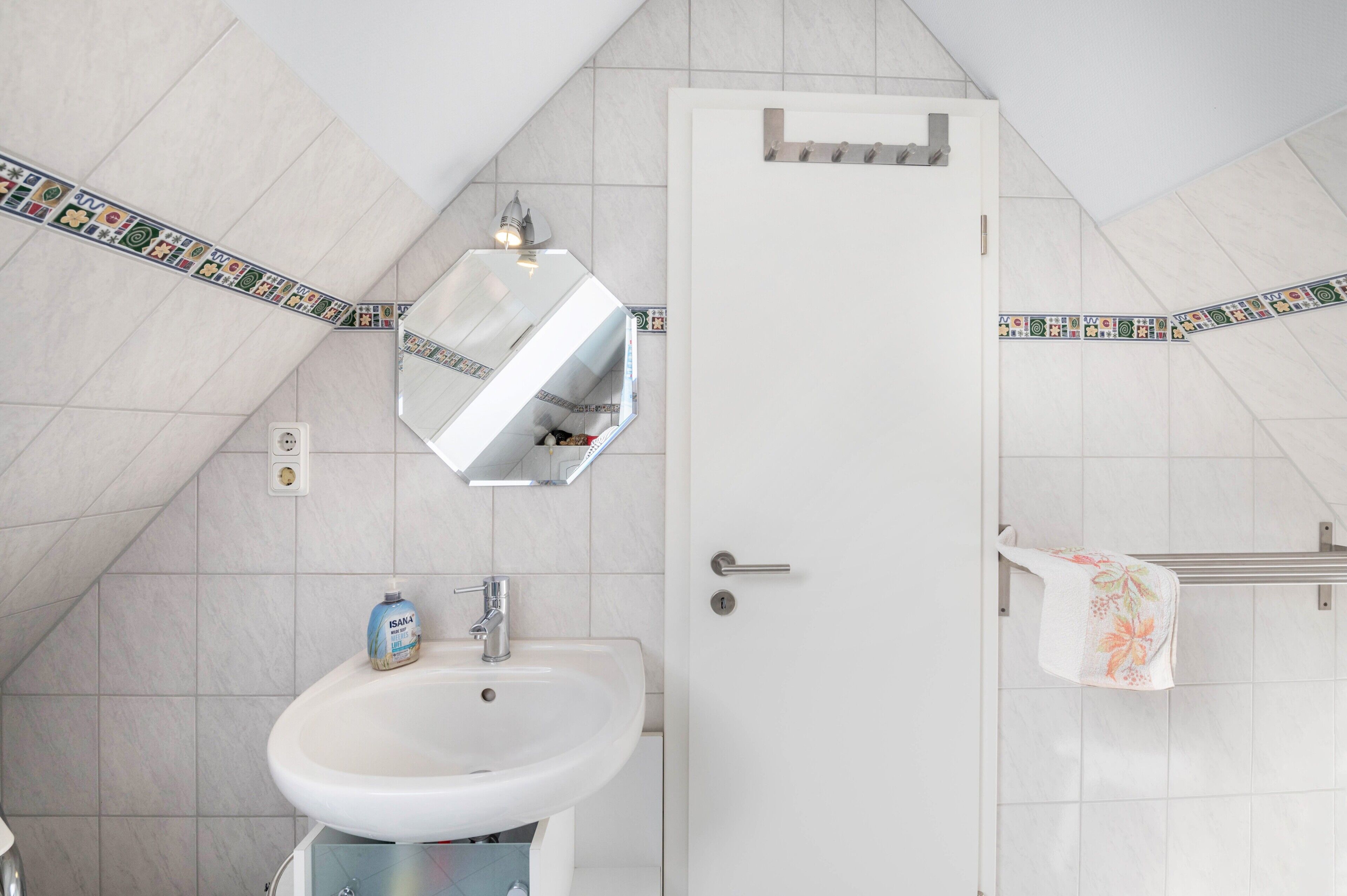 Een badkamer met een wit wastafelmeubel, een spiegel, een handdoekrek en een deur.