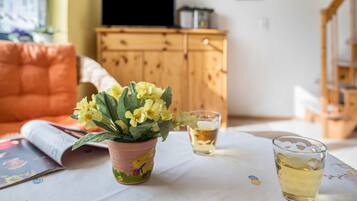 Ein Zimmer mit einem Holzkasten, einem Fernseher, einer Topfpflanze und einem Tisch mit einem Glas und einem Buch.