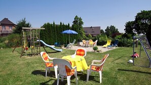 A backyard with a play area, including a slide and climbing structure, and a seating area with chairs and a table.