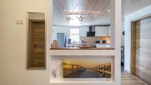 Cocina moderna con detalles de madera, una lámpara colgante y un cuadro de un sendero al atardecer.