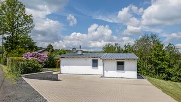 A small, single-story building with a paved driveway and a garden area with flowering plants.