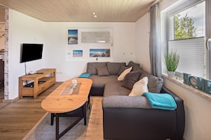 Una sala de estar moderna con un sofá, una mesa de centro de madera, un televisor de pantalla plana y obras de arte en la pared.