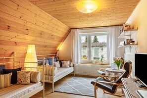 Une pièce chaleureuse avec un plafond en bois, un lit avec des oreillers, une chaise, une table avec une lampe et une fenêtre donnant sur un beau paysage.