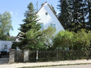 Un edificio blanco con techo inclinado, rodeado de árboles y una valla de madera.