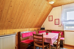 Un comedor acogedor con techo de madera, una mesa con mantel a cuadros, sillas de madera y un banco con cojines rojos.