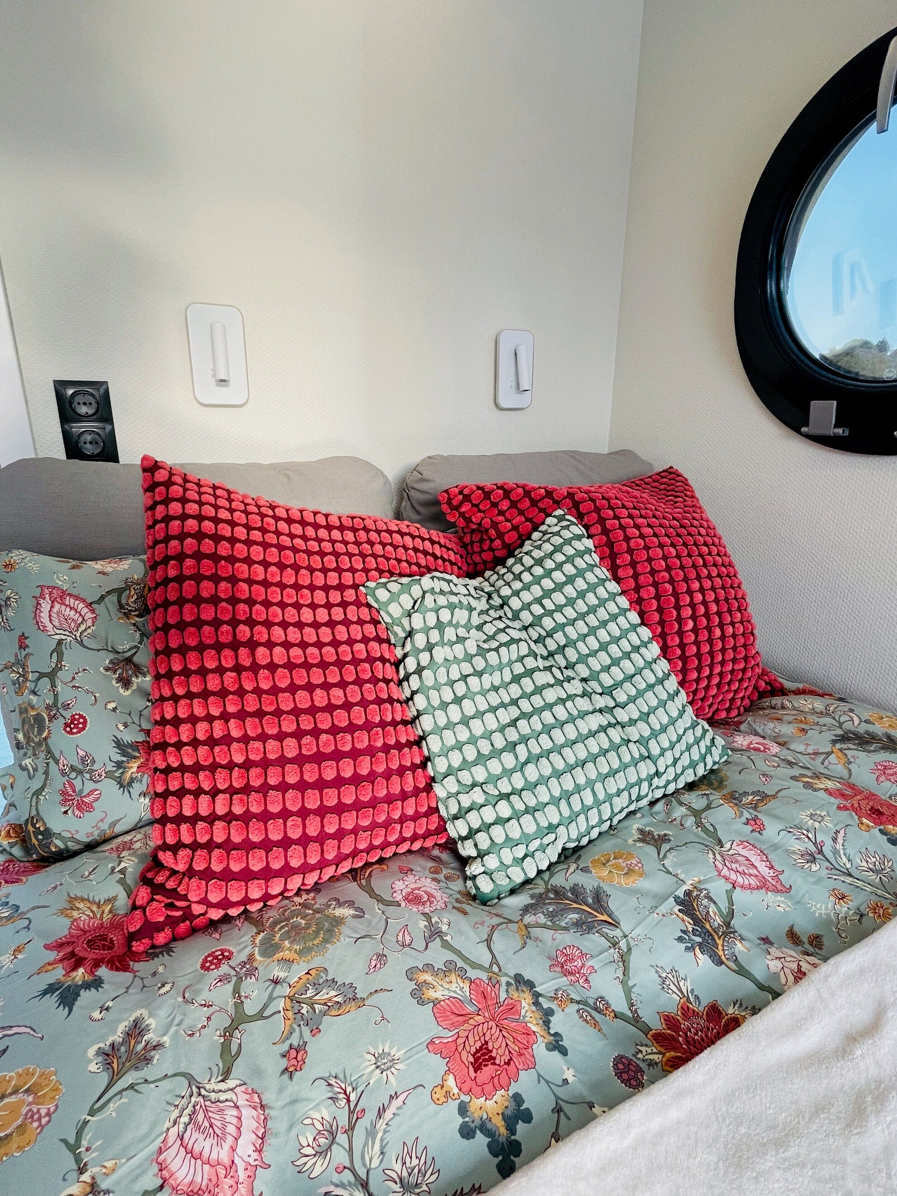 A bed with floral bedding and red and green patterned pillows.