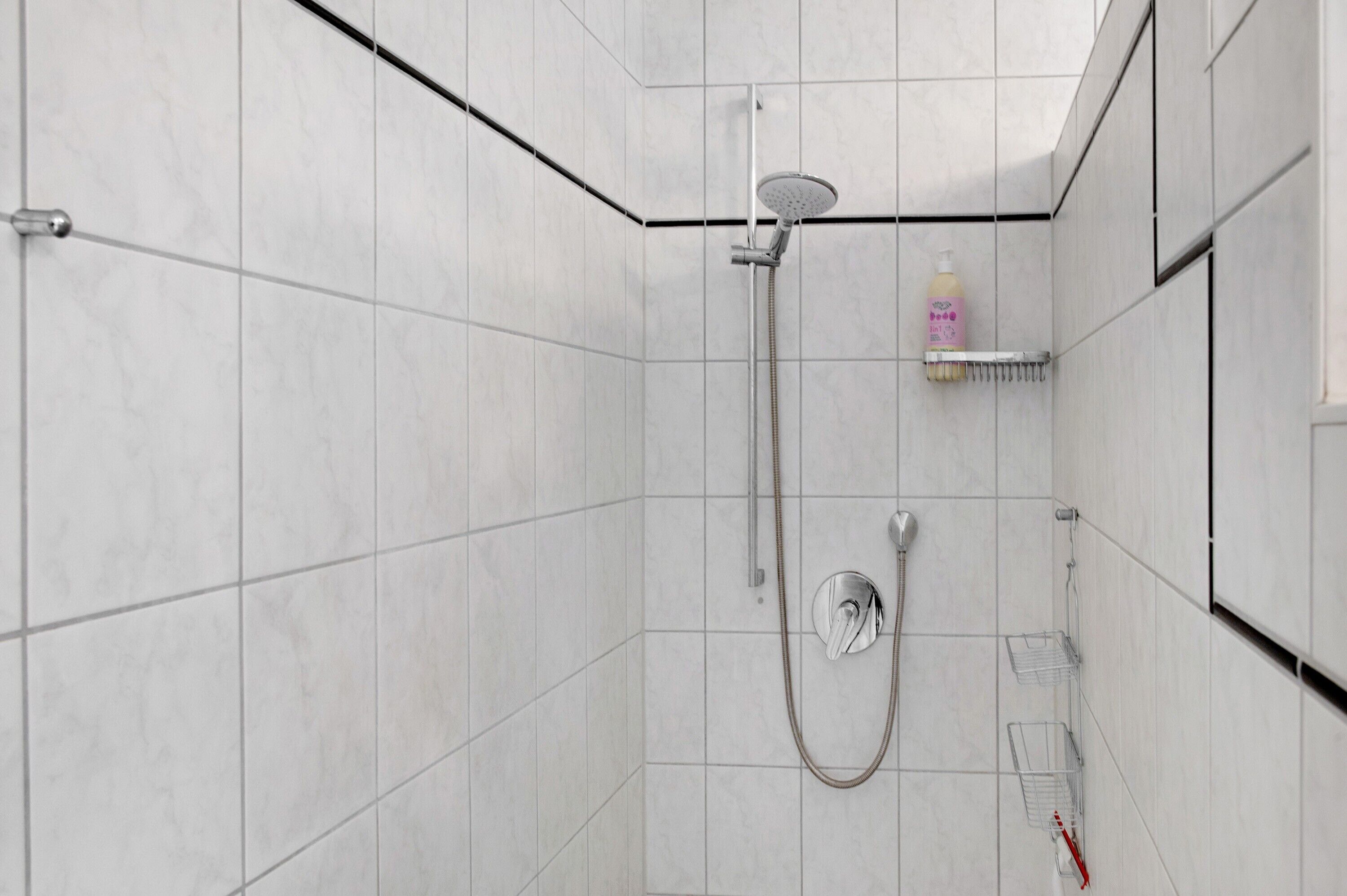 Eine moderne Dusche mit Duschbrause, Wandarmatur und Seifenspender.