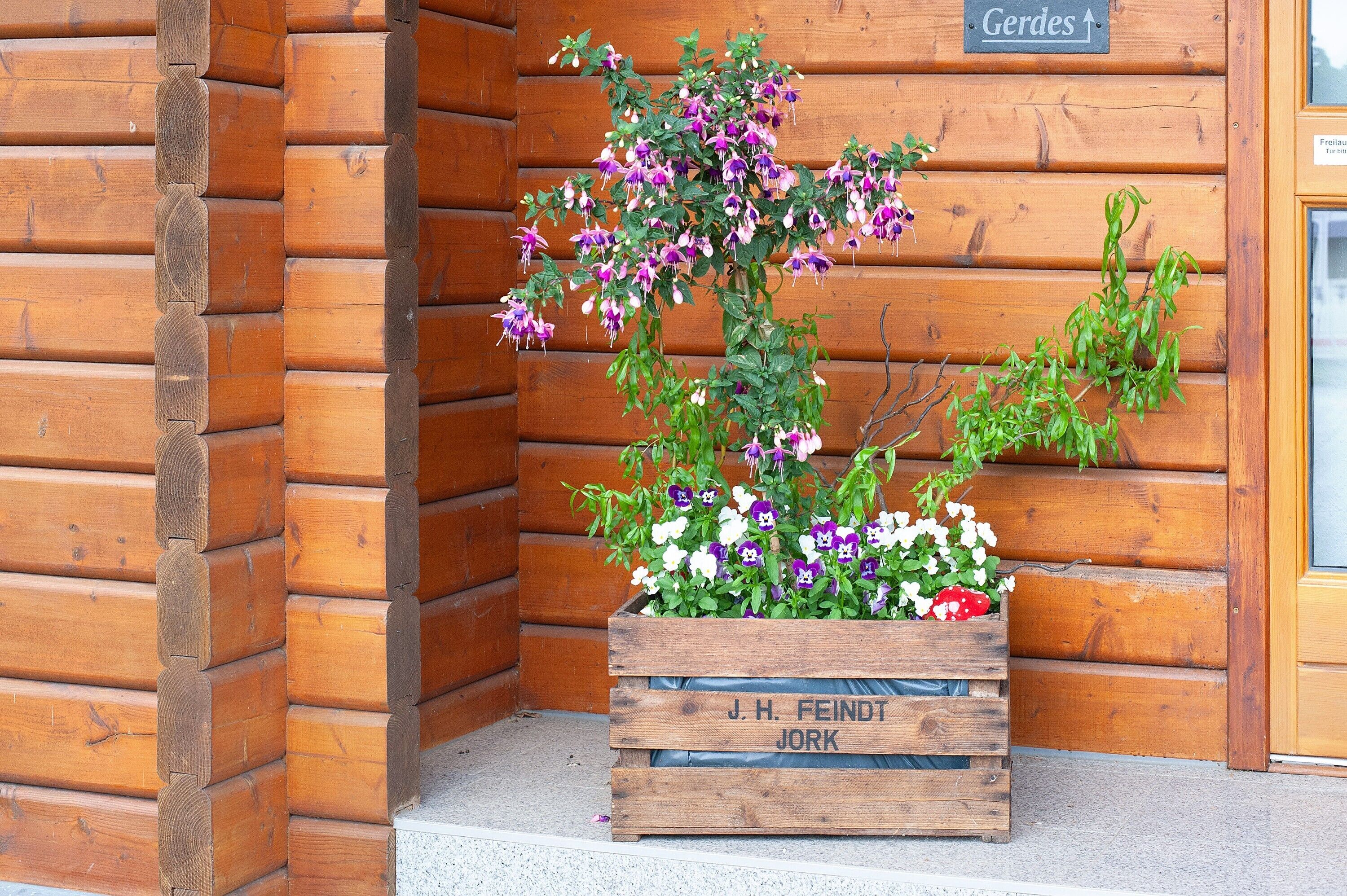 Una cabaña de troncos de madera con una jardinera de madera con flores y una etiqueta que dice 'J. H. Feindt Jork'.