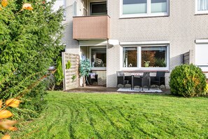 Een tweelaags gebouw met een balkon, een klein terras met tuinmeubilair en een verzorgd gazon.