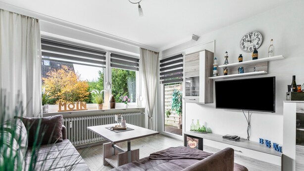 A modern living room with a sofa, a coffee table, a TV, and a window with a view of trees.