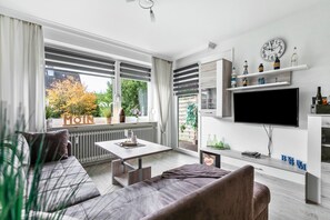 Een moderne woonkamer met een bank, een salontafel, een televisie en een raam met uitzicht op bomen.