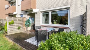 A residential building with a patio area featuring a table and chairs, a wooden deck, and a brick facade.