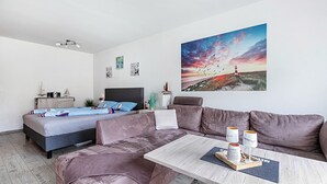 A modern bedroom with a bed, a sofa, a coffee table, and a painting of a sunset.