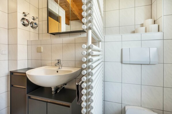 Une salle de bain avec un lavabo blanc, un miroir, un porte-serviettes et des toilettes.