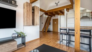 Una sala de estar moderna con televisor, vigas de madera, una escalera y una zona de cocina.