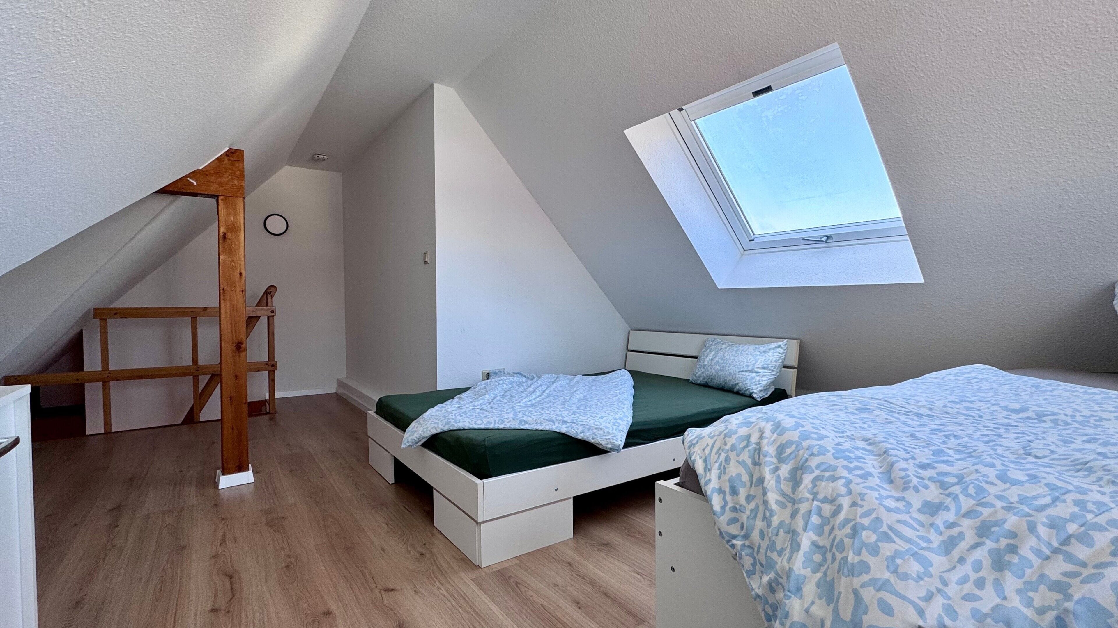 A bedroom with a sloped ceiling, a skylight, a bed with a green bedspread, a bedside table, and a chair.