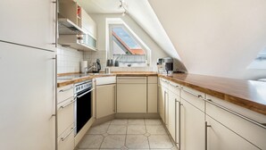 Una cocina con horno empotrado, cafetera y ventana con vista a un edificio de tejados rojos.
