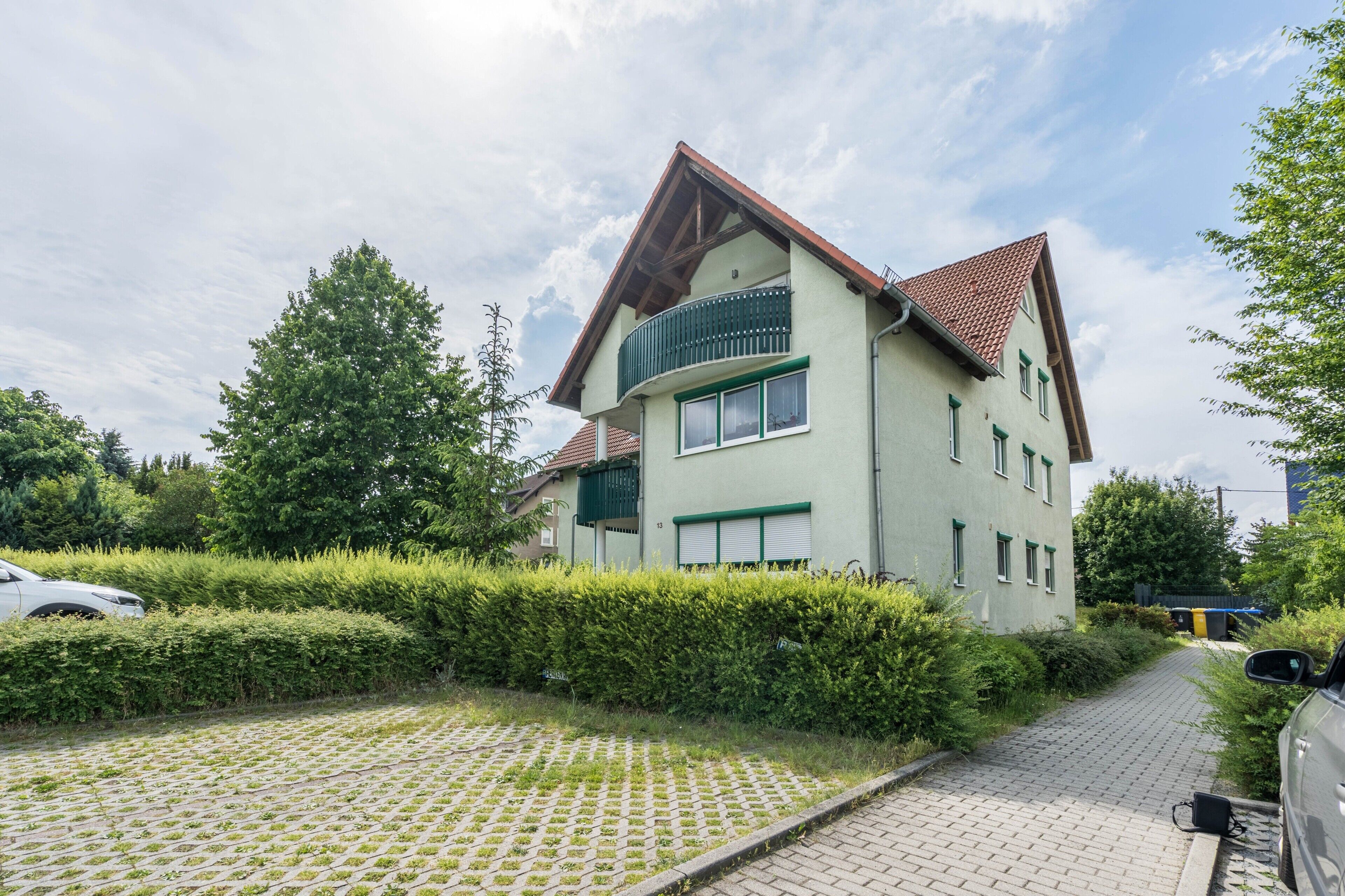 Une maison à deux étages avec un balcon, une allée pavée et une haie.