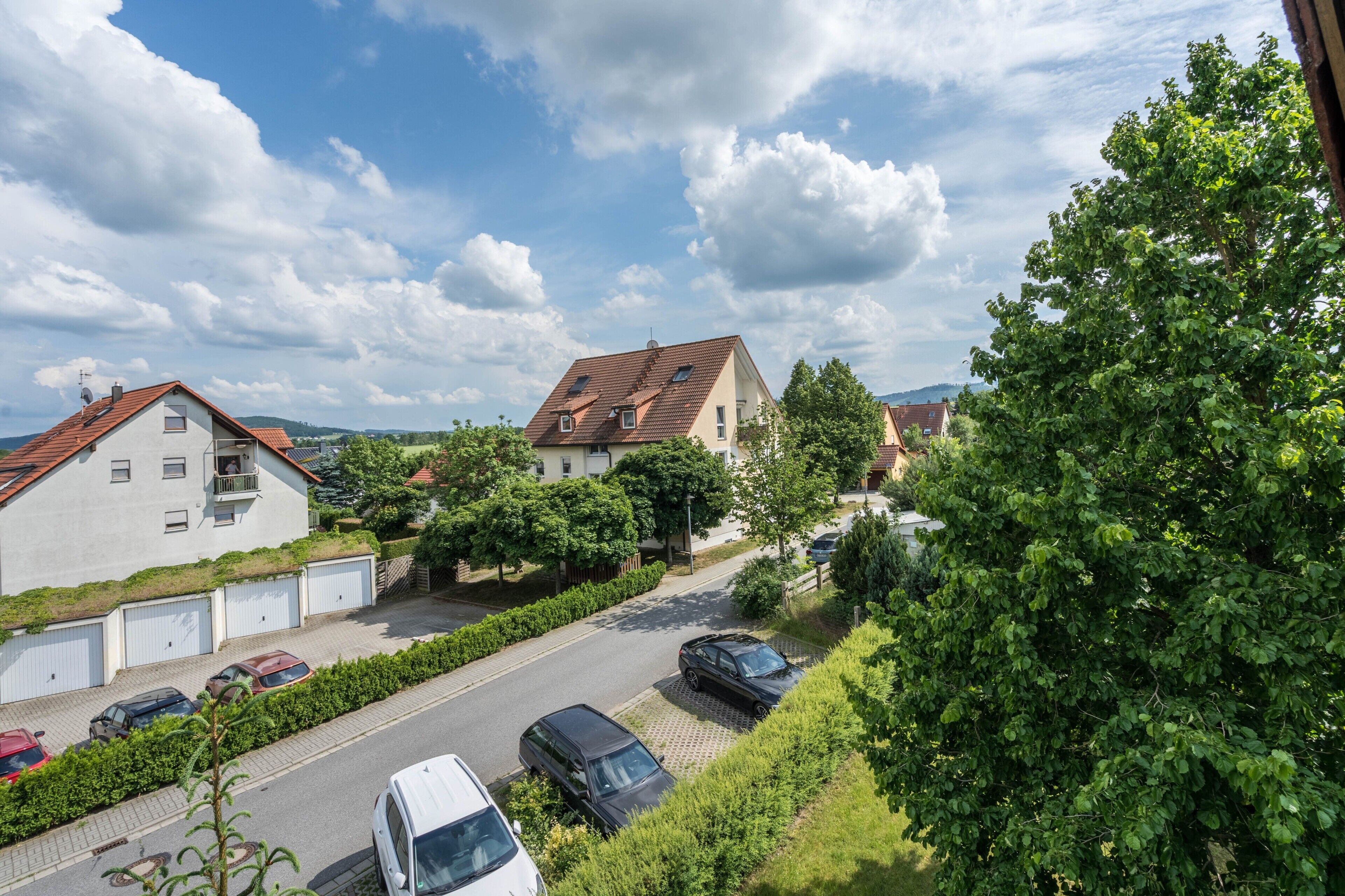 Une rue résidentielle bordée de maisons, de voitures garées et d’une végétation luxuriante.