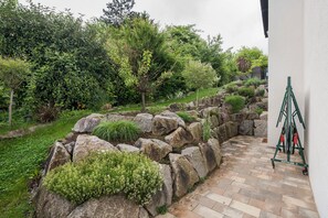 A garden with a stone retaining wall, a Kettler 5 wheeled cart, and a white building. - Apartment "Murgperle" with Mountain View, Private Terrace & Wi-Fi (Gernsbach)
