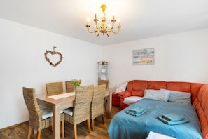 Quarto com mesa de jantar, cadeiras, sofá, cama, lustre, decoração em formato de coração e pôster motivacional.