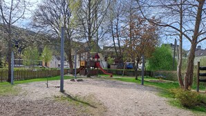Une aire de jeux avec un toboggan et des structures d’escalade, entourée d’arbres et d’une clôture.
