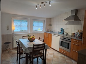 A kitchen with a dining table, chairs, a fruit bowl, a coffee maker, and a stove. - Apartment 'Les Papillons' with Mountain View, Shared Terrace and Wi-Fi (Tennenbronn)