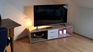 Un téléviseur posé sur un meuble en bois, avec une télécommande, un petit tiroir et un porte-bougie.