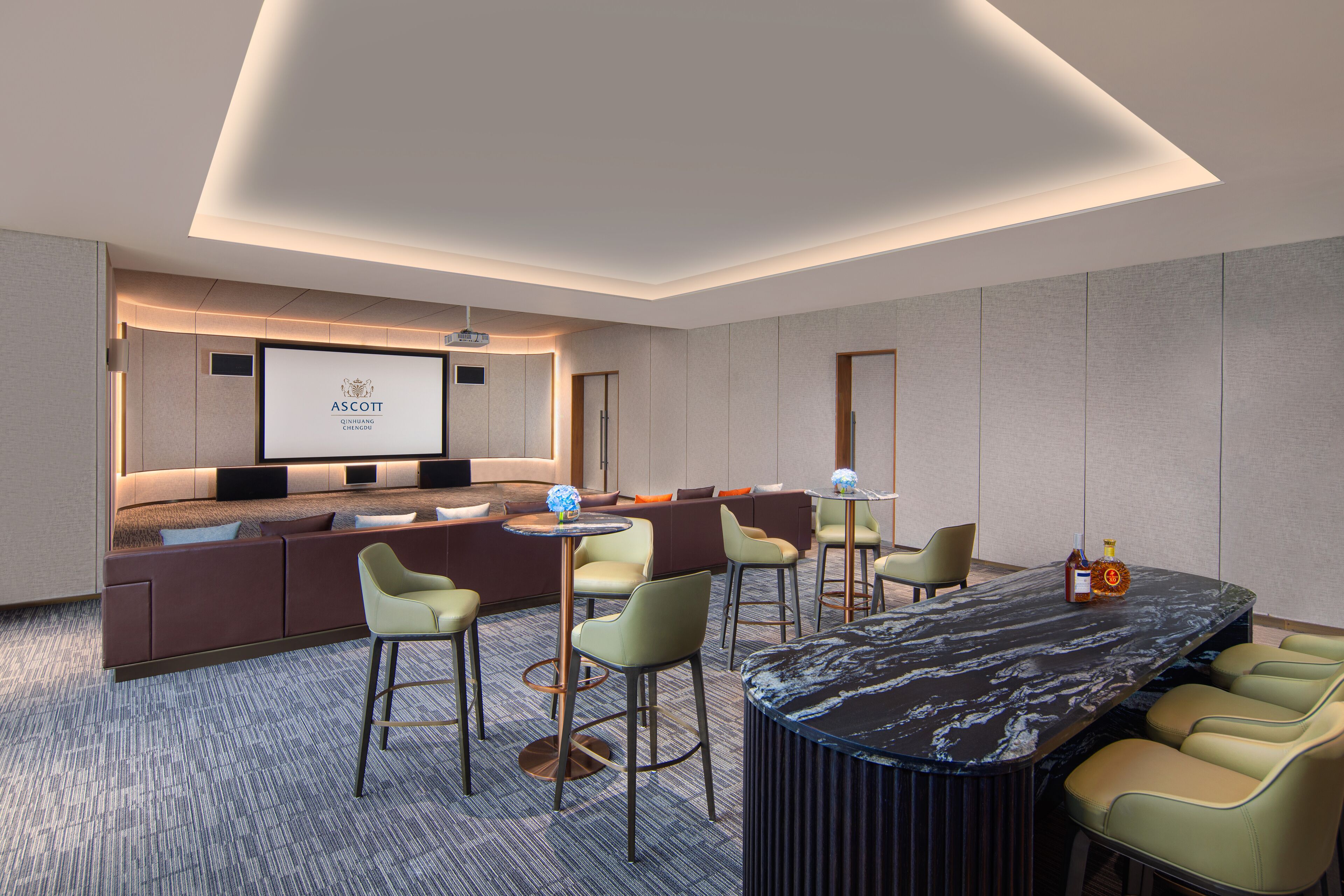 A modern hotel room with a large seating area, a bar, and a television screen displaying the ASCOTT logo.