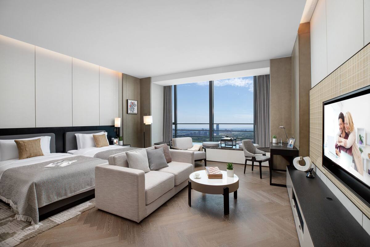 A modern hotel room with a large bed, a sofa, a coffee table, and a TV.