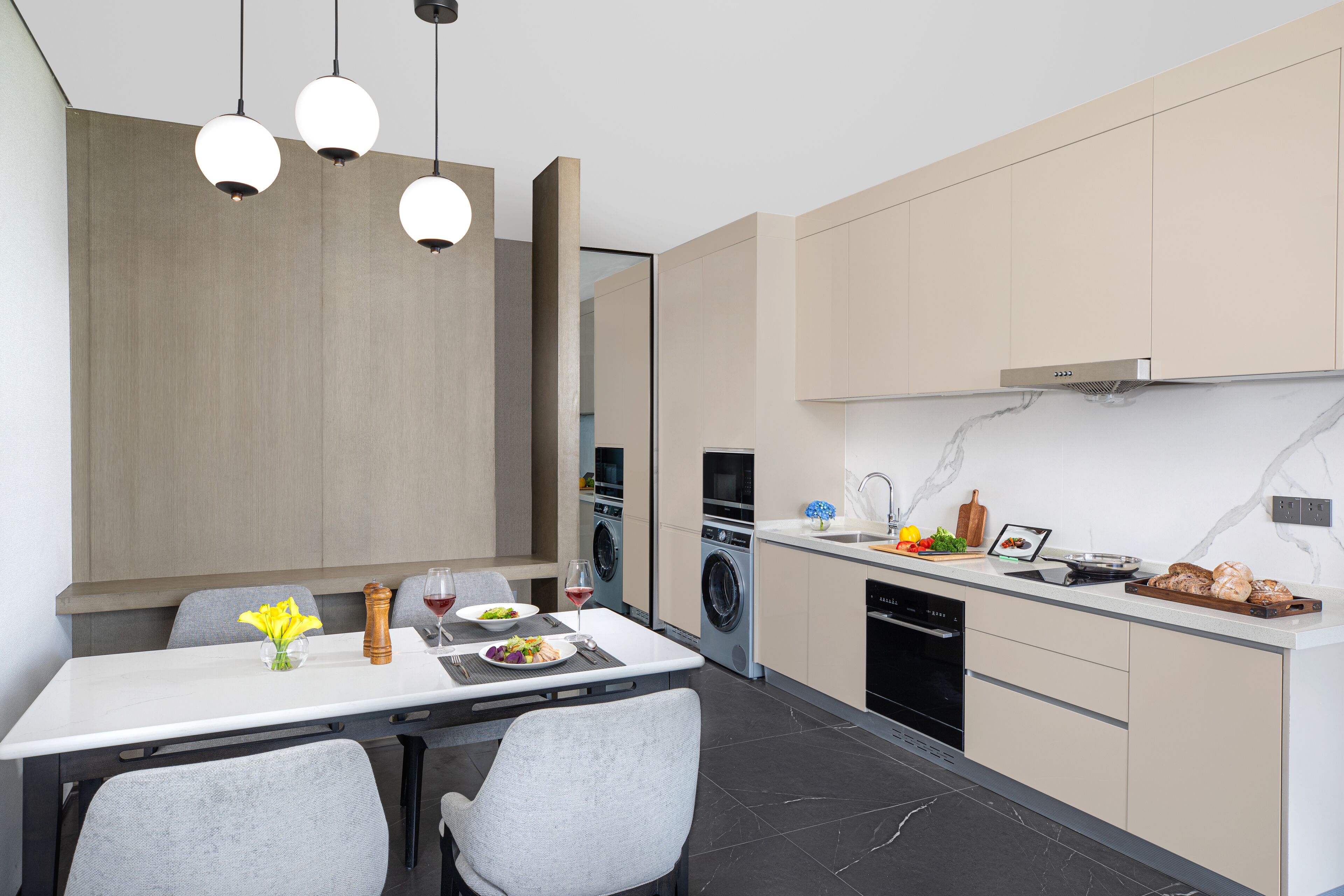 Una cocina moderna con comedor, que presenta una encimera blanca, sillas grises y una mesa de comedor de madera.
