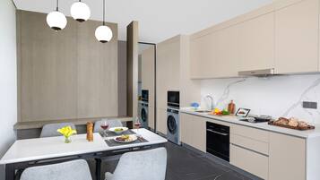 Una cocina moderna con comedor, que presenta una encimera blanca, sillas grises y una mesa de comedor de madera.