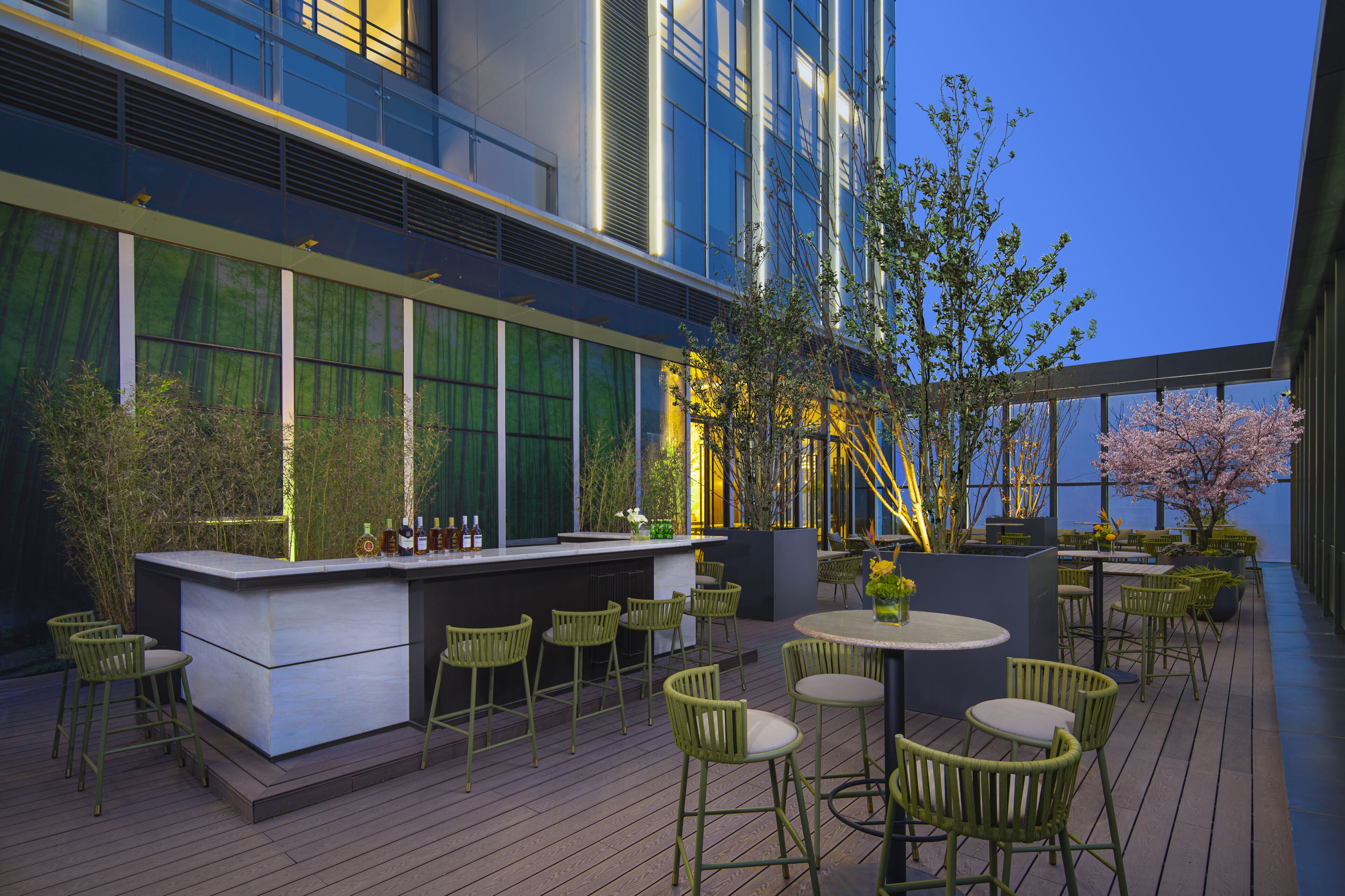 An outdoor bar area with a modern design, featuring a bar counter, multiple seating options, and a view of the cityscape.