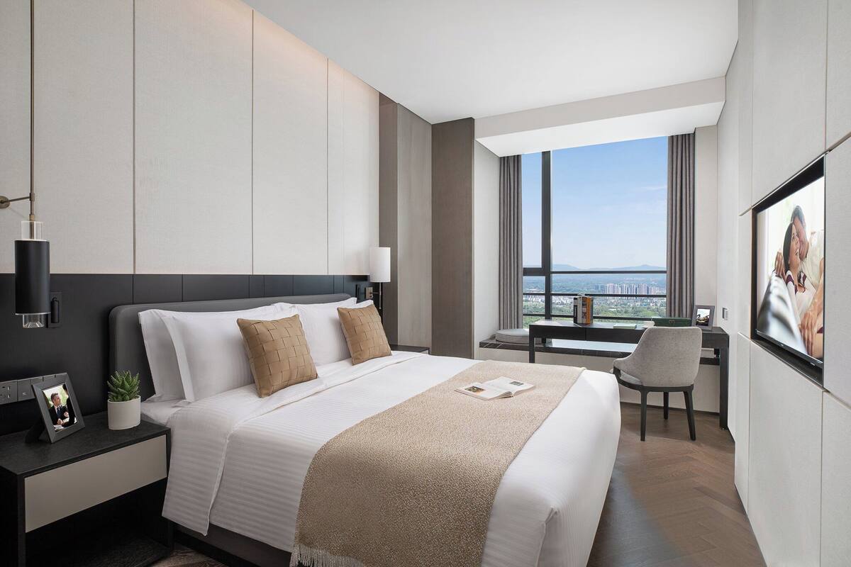 A modern hotel room with a large bed, a desk, and a view of the city.
