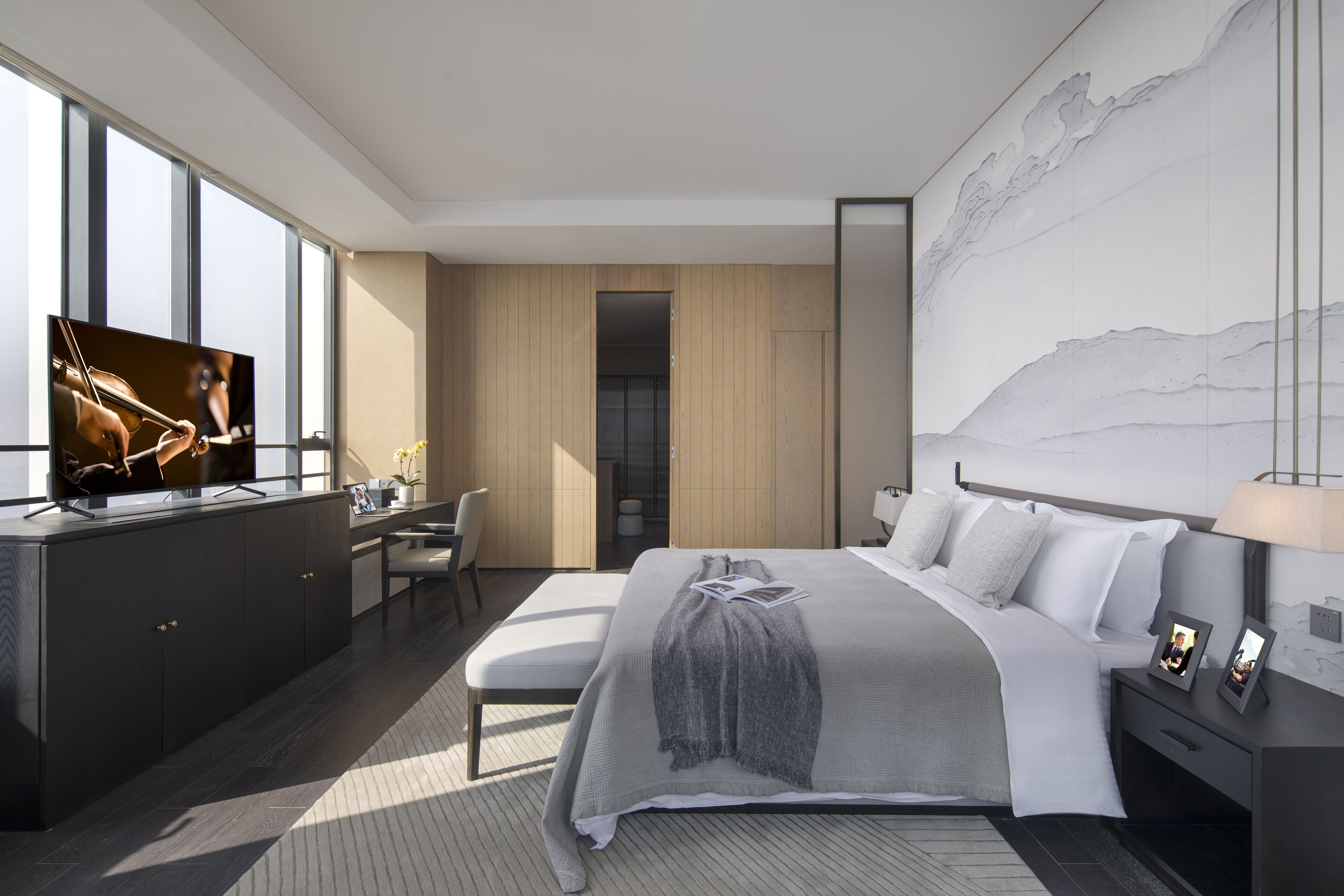 Une chambre d’hôtel moderne dotée d’un grand lit, d’un bureau avec une télévision, d’une grande fenêtre et d’un mur au motif rappelant le marbre.