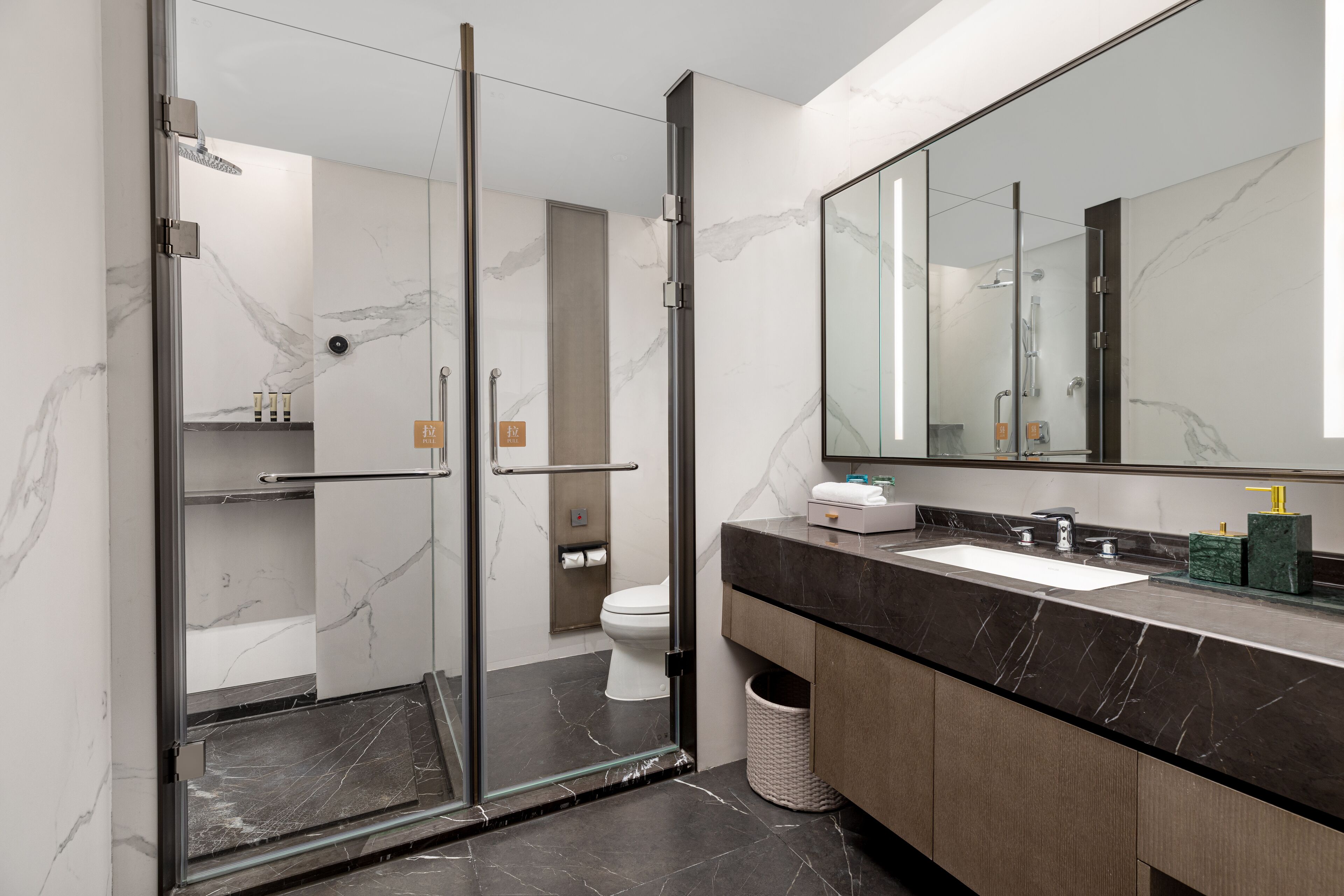 A modern bathroom with a glass-enclosed shower, a large mirror, and a marble-tiled floor.