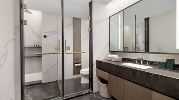 A modern bathroom with a glass-enclosed shower, a large mirror, and a marble-tiled floor.