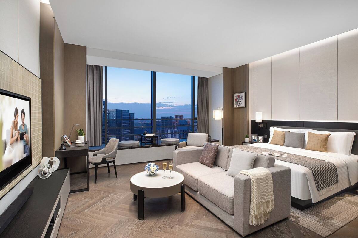 A modern hotel room with a large bed, a sofa, a TV, and a desk.